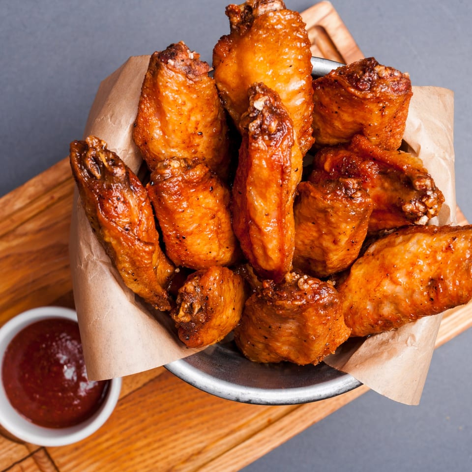 A metal bowl filled with crispy, golden-brown chicken wings and a side of red dipping sauce.