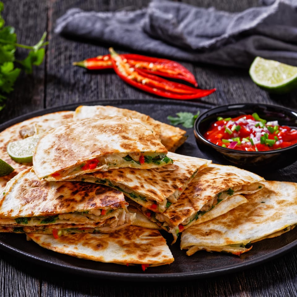 Guac Island Mexican Grill's quesadillas with salsa, lime, and chili peppers on a dark wooden table.